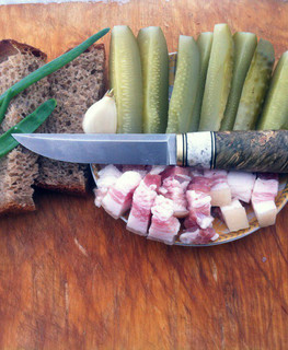 нож финского типа лежит на тарелке с салом, огурчиками и хлебом